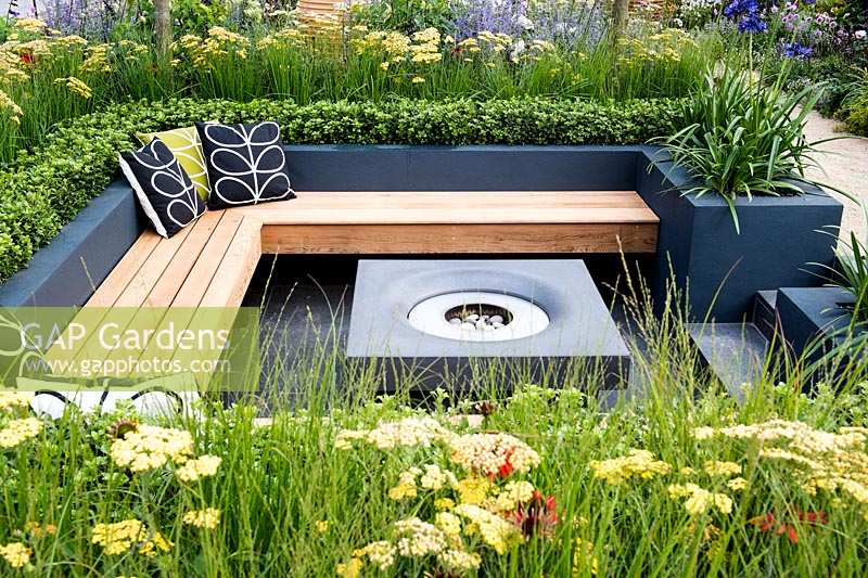 Modern seating area with fireplace surrounded by raised flower beds with 
Achillea, Agapanthus and Buxus sempervirens. 
Best of Both Worlds garden  
RHS Hampton Court Palace Flower Show 2018