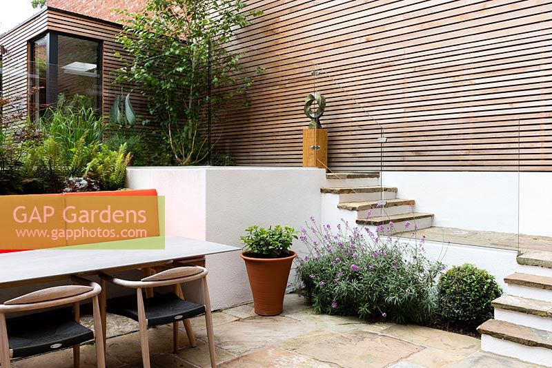 Paved steps leading down to sunken seating area in modern multi-level urban garden. 