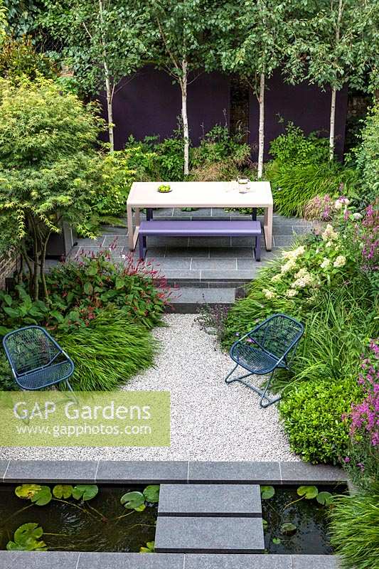 Overview of table and bench and modern narrow garden pond in small urban garden.  Garden design by John Davies Landscape.