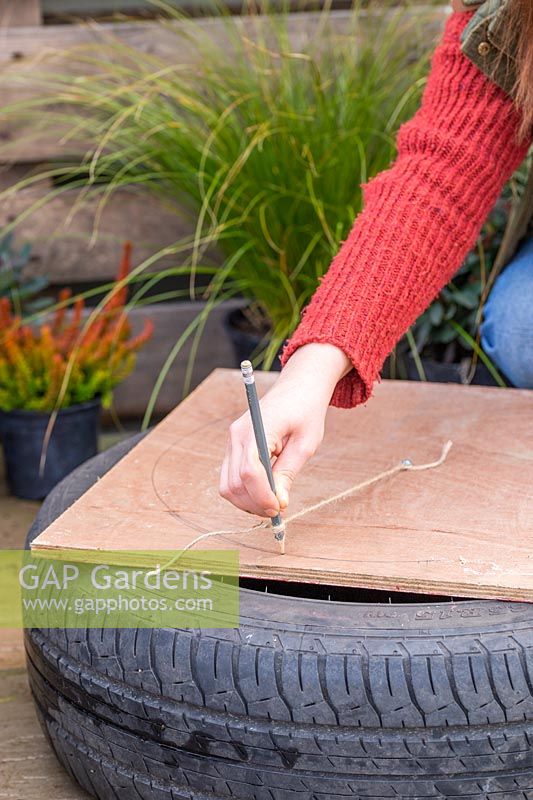 Woman marking out circle on sheet of hardboard, to create base for tyre planter.