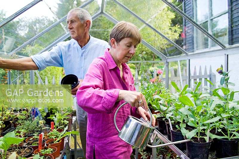 Freda and Barry Waldapfel tending and watering plants in their greenhouse.