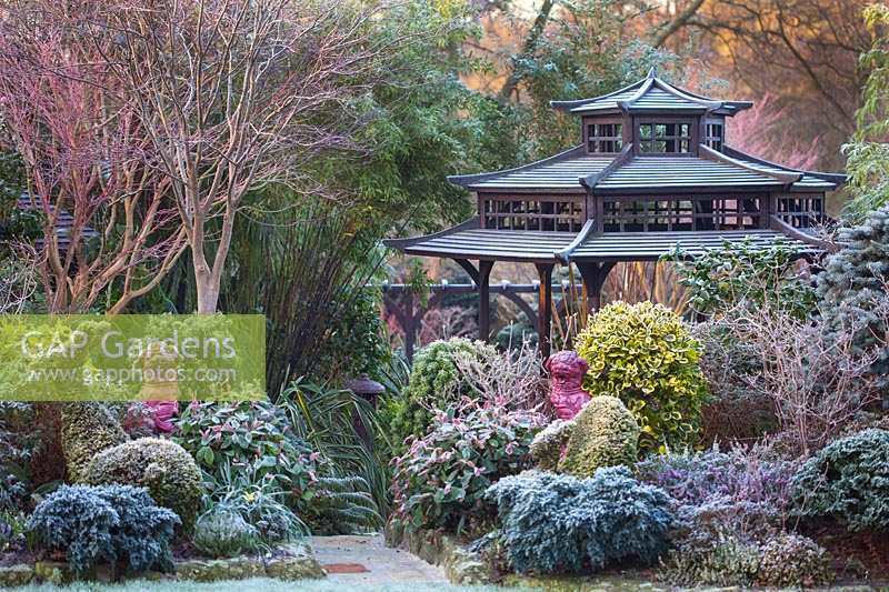 Japanese Tea House-style gazebo in frosted garden, with oriental statuary and shrubs and trees.