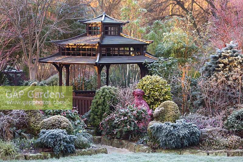Japanese Tea House-style gazebo in frosted garden, with oriental statuary and shrubs and trees.