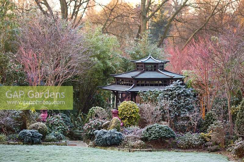 Japanese Tea House-style gazebo in frosted garden, with oriental statuary and shrubs and trees. The Four Seasons Garden, UK. 
