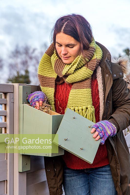 Woman removing debris from wooden nesting box in winter.