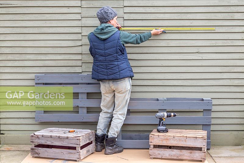 Woman measuring and marking where to drill holes for fixing pallet. 