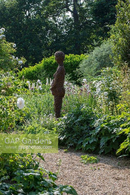 Willow sculpture of figure by Helen Colletta, standing amongst white flowering plants.  