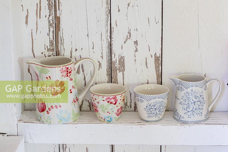 Floral jugs and mugs displayed on white wooden wall in shop. 