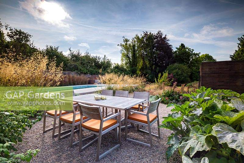 Dining table and chairs with view to swimming pool, in contemporary garden near Winchester, Hants, UK. Designed Elks-Smith Garden Design. 