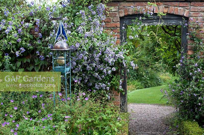 Sundial surrounded by purple flowering perennials including Clematis 'Perle D'Azure' at Wollerton Old Hall, Market Drayton, UK.