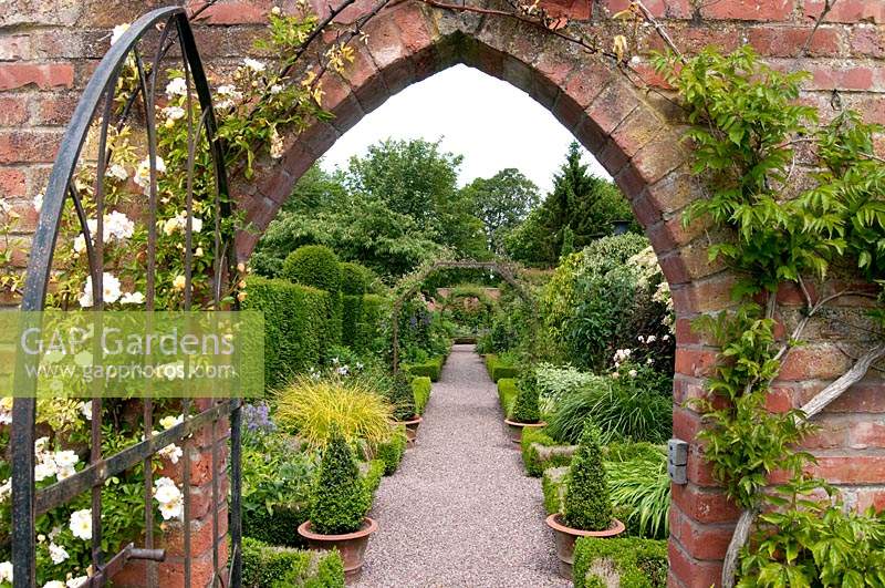 View through brick archway and gate to Buxus - Box edged borders of the Long Border at Wollerton Old Hall, Shropshire, UK.
