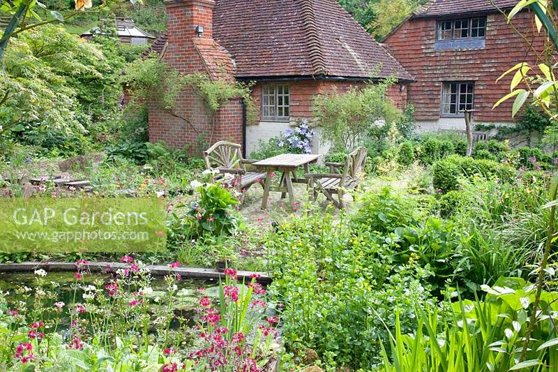 Rustic table and chairs on patio in informal cottage garden. Copyhold Hollow, Sussex, UK. 