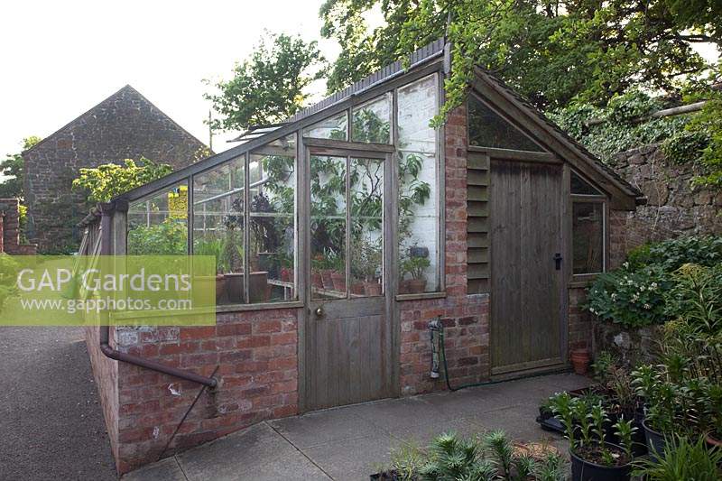 Outside of a combined greenhouse and shed with an entrance for each, a brick 
structure with wood

