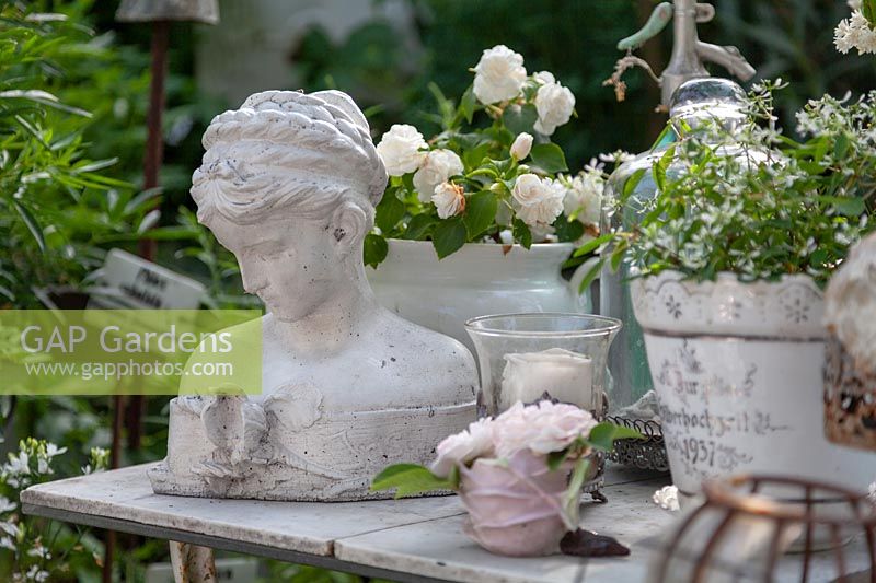 Collection of white-themed vintage items on a table. These include a bust of 
woman's head and potted plants with white flowers.
