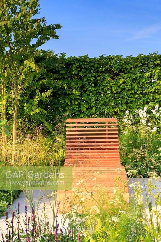 Wooden slatted shaped recliner surrounded by naturalistic planting. 'Molecular Garden', designed by Denis Kalashnikov and Ekaterina Bolotova. Malvern Spring Festival, 2017. 