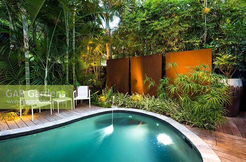 Tropical garden with swimming pool, deck, seating area and foliage planting, all screened with walls and plants