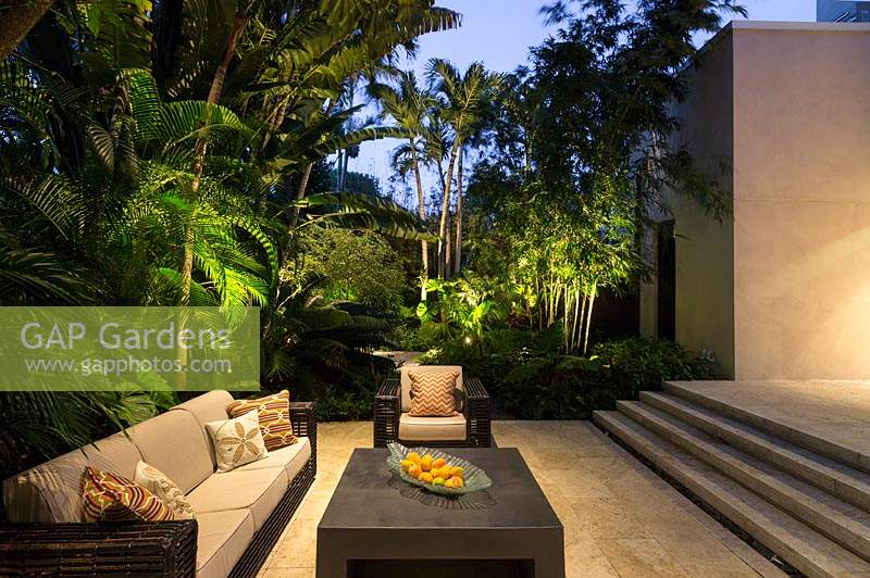 Modern seating area surrounded by lush tropical planting at night. Florida, USA. Garden design by Craig Reynolds Landscape Architecture.
