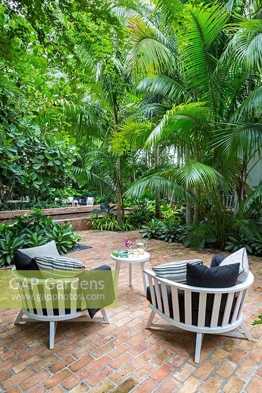 Two low wooden garden chairs in tropical garden. Key West Classic Garden, designed by Craig Reynolds. Key West, Florida, USA.