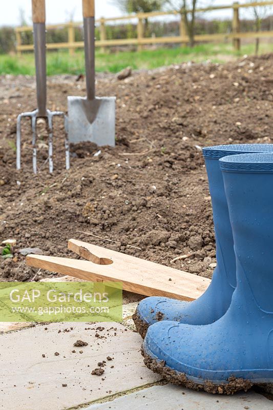 Muddy boots and boot Jack on paving near soil and digging tools