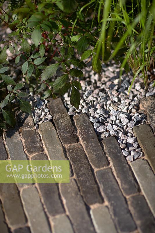 Brick pathway edged with coarse stones in show garden. The South West Water Green Garden, designed by Tom Simpson, Sponsored by South West Water, RHS Hampton Court Flower Show, 2018.
