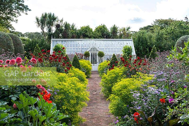 A brick path, leading through a restored Victorian walled kitchen garden to a greenhouse, is edged with clumps of Euphorbia ceratocarpa, interspersed with dahlias, asters, Verbena bonariensis and clipped bay trees.