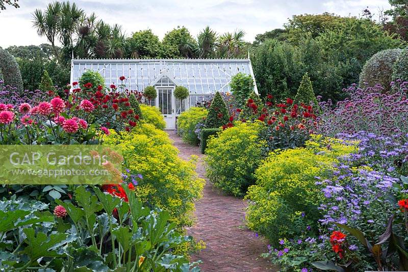 A brick path, leading through a restored Victorian walled kitchen garden to a greenhouse, is edged in clumps of Euphorbia ceratocarpa, interspersed with dahlias, asters, Verbena bonariensis and clipped bay trees.