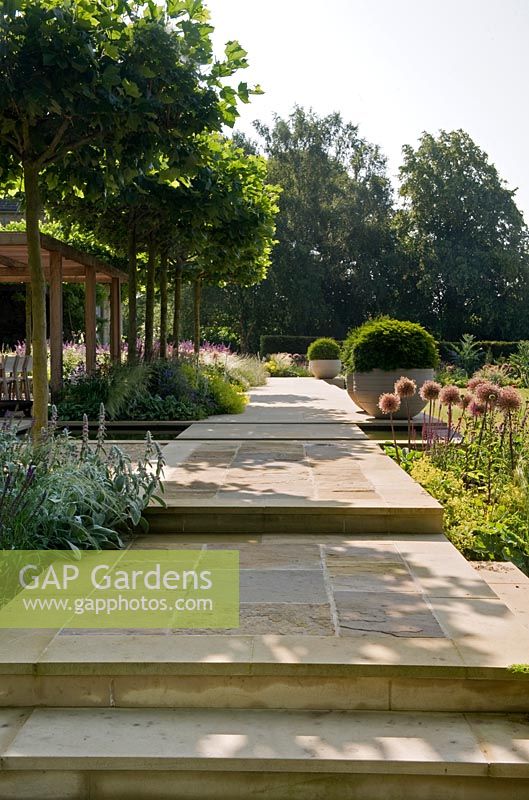 Multi-level paved pathway, with perennial borders and  large pots of topiary evergreens. 