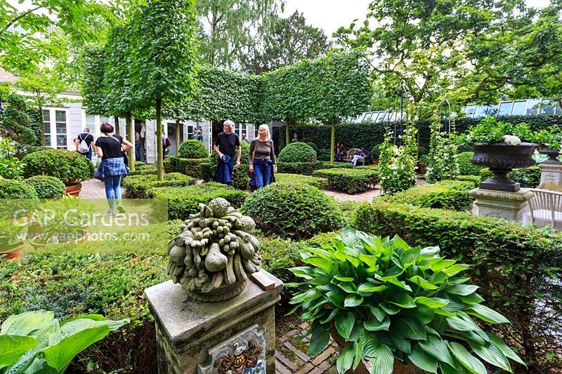 Visitors enjoying one of the privately owned gardens along the Keizersgracht canal, which has been designed for a tranquil atmosphere with foliage plants and only white flowers. Amsterdam, The Netherlands. 