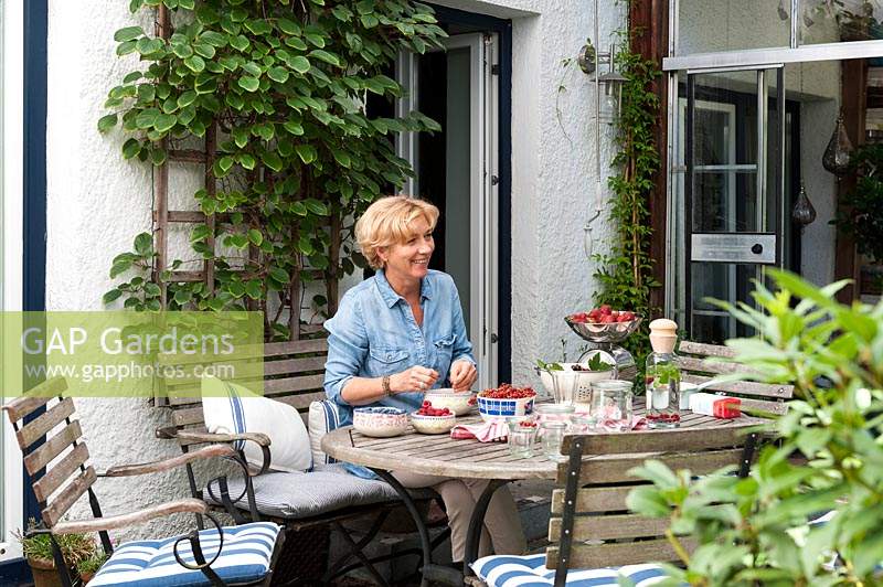 Woman sitting at garden table with bowls of freshly harvested fruit in bowls 