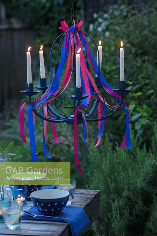 A ribbon chandelier over a dining table at dusk with all the candles lit. 