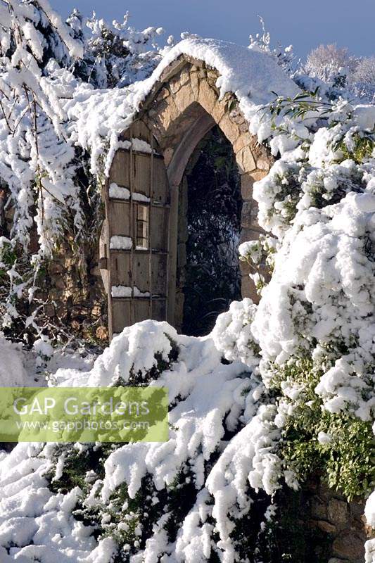 Stone gate in the snow at Burrow Farm Garden, Dalwood, Devon, UK. 