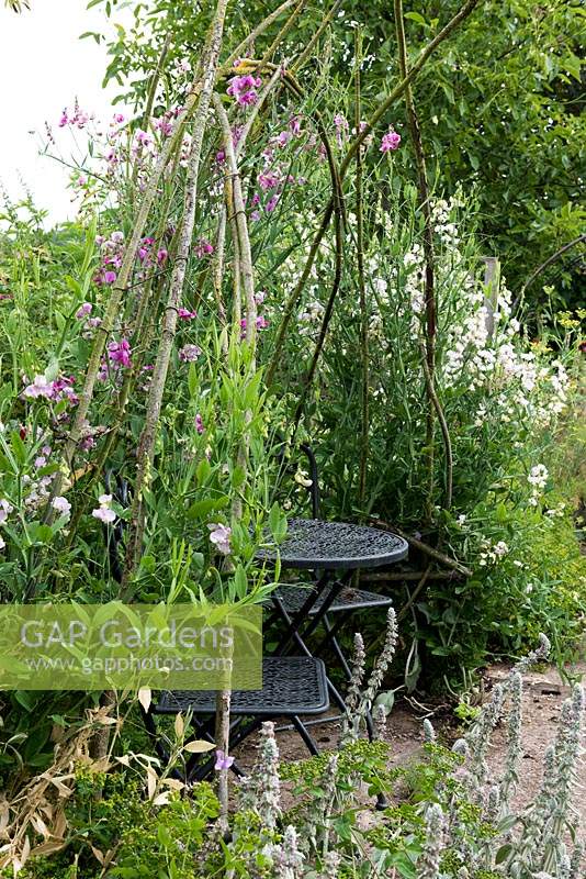 A small table and chairs is enclosed in a rustic arbour smothered in sweet peas.