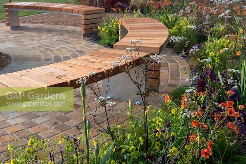 Curved border next to a wooden bench on a brick patio, - The Redshift, RHS Malvern Spring Festival 2019