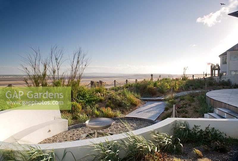 Curved seating around fire pit in seaside garden, with view to beach. 