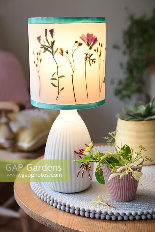 Upcycling an old plain lampshade with pressed flowers from the garden. Finished project with lampshade attached to a base on a table indoors