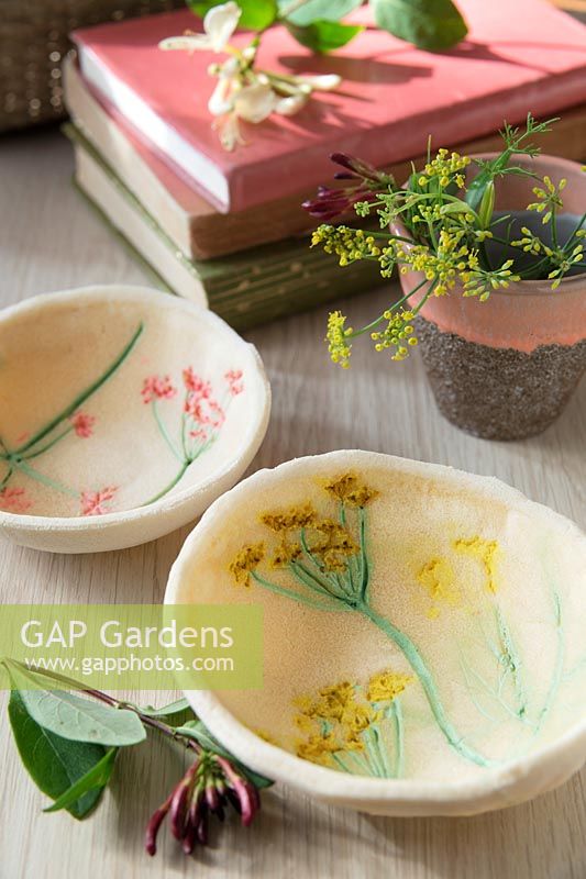 Small bowls, made out of salt dough and decorated with painted flower imprints, on a table with books and fresh flowers