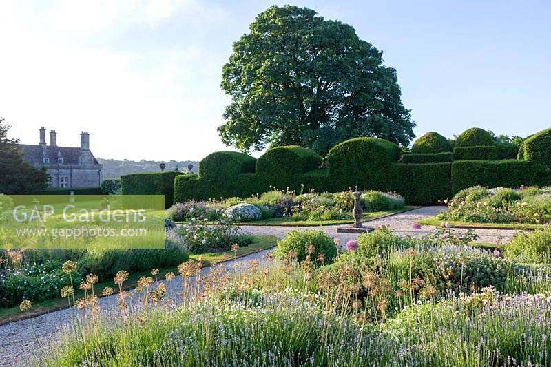 Miserden Park, Gloucestershire, summer, with spectacular views over a deer park and rolling Cotswold hills beyond. The formal parterre style garden with allium seed heads in summer.