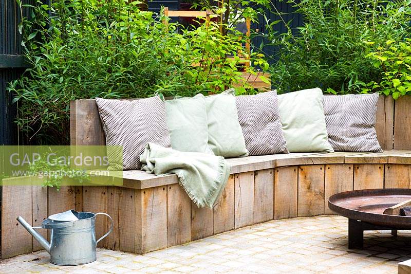 Seating area with fire pit and round wooden bench surrounded by Cornus alba 'Sibirica'. 