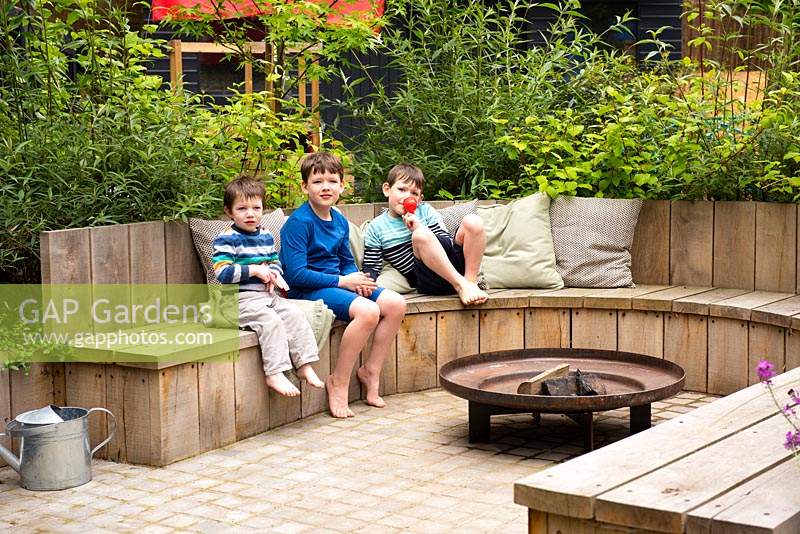 Children seating on the bench by fire pit in the garden.
