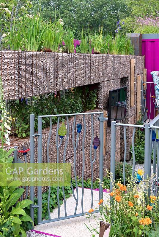 The Montessori Centenary Childrens Garden: Pebble filled gabion wall and metal entrance gate. Sponsors: Montessori centre International. Rhs Chelsea flower show 2019.