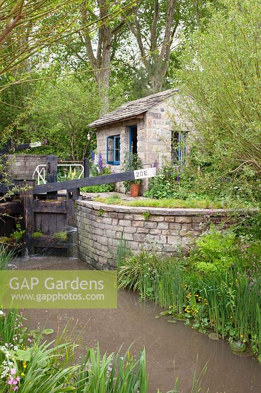 The Welcome to Yorkshire Garden. View of the lock and keeper's office with canal and water's edge planting which includes: Caltha palustris - Marsh Marigold and Iris pseudacorus. Sponsor: Welcome to Yorkshire