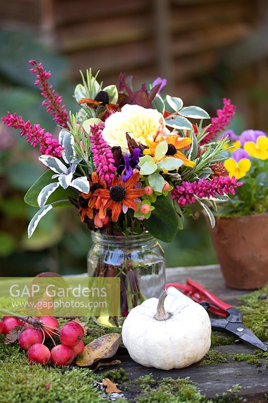 Posy or Tussie Mussie with a colourful  mix of flowers and foliage on table with Malus - Crabapple - fruits, moss and white Winter Squash