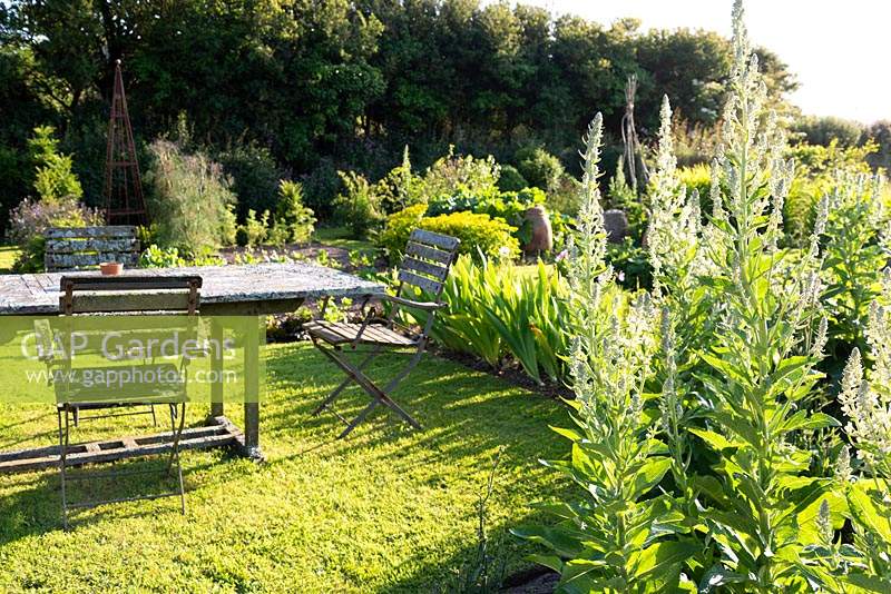 Dining area in the kitchen garden with lichen encrusted table and chairs at Sea View, Cornwall, UK in June.