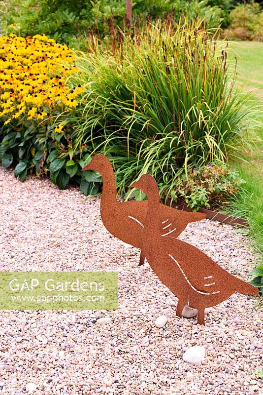Decorative metal cut out geese in a gravel garden with Rudbeckia fulgida var. sullivantii 'Goldsturm' behind.