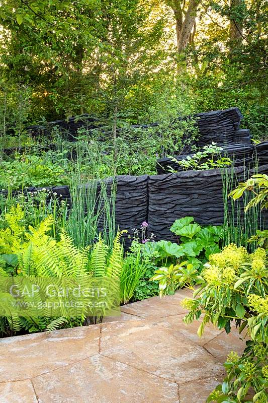 Burnt oak timbers surrounded by mixed foliage planting in woodland garden.  RHS Chelsea Flower Show 2019 