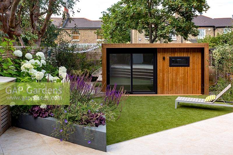 London contemporary garden - view of garden from house towards artificial lawn with sun lounger, garden room or gym and lower wood deck area.