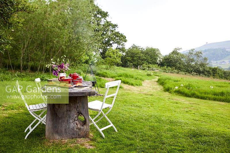 Rustic wooden table and chairs, table set for breakfast - fire place with cooking facilities in background and view to landscape