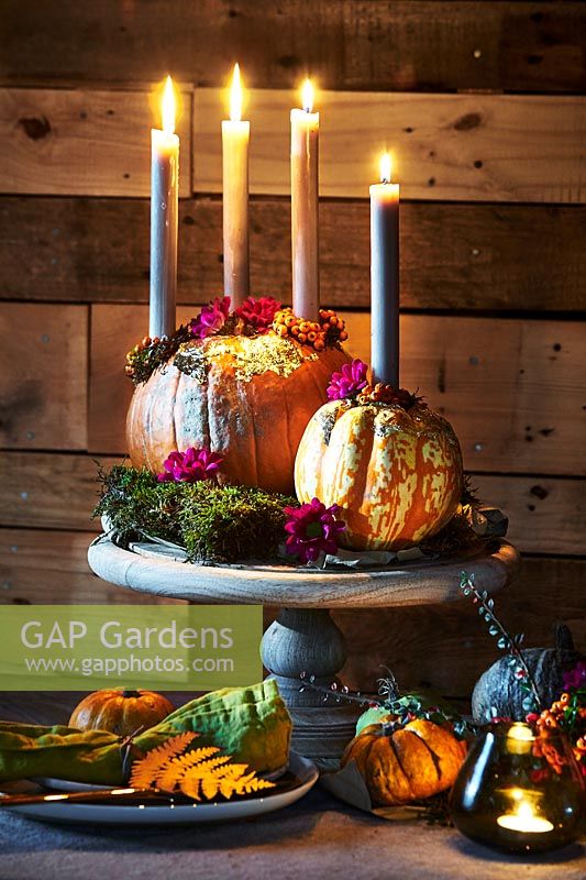 Atmospheric arrangement with candles, pumpkins and flowers on a wooden stand.