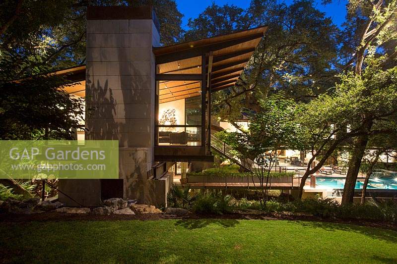 Contemporary house and garden, with trees and outdoor living area, lit up at night