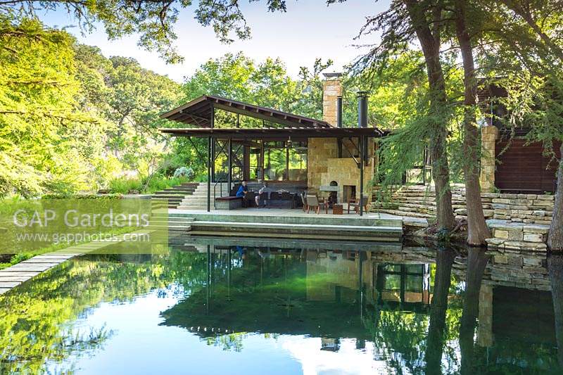 View across creek to terrace and outside seating area at Mill Creek Ranch in Vanderpool, Texas designed by Ten Eyck Landscape Inc, July.